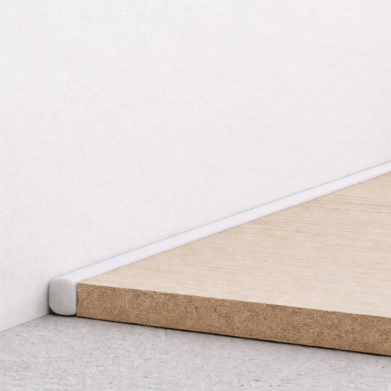Close-up of a compressible PE foam strip in the expansion gap between a white wall and floor.