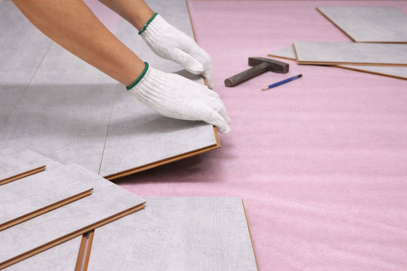 Person wearing gloves installiing Waterblock X Kasu light grey floor panels on a pink underlay with tools nearby